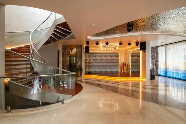 Panoramic view of double-height entrance atrium with curved marble floor inlays, spiral staircase, and metallic ceiling