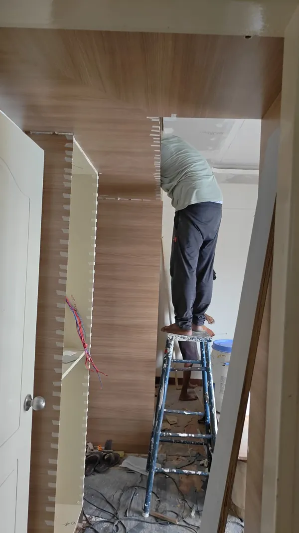 Carpenter applying and taping edge laminate wrapping across structural ceiling drop beam