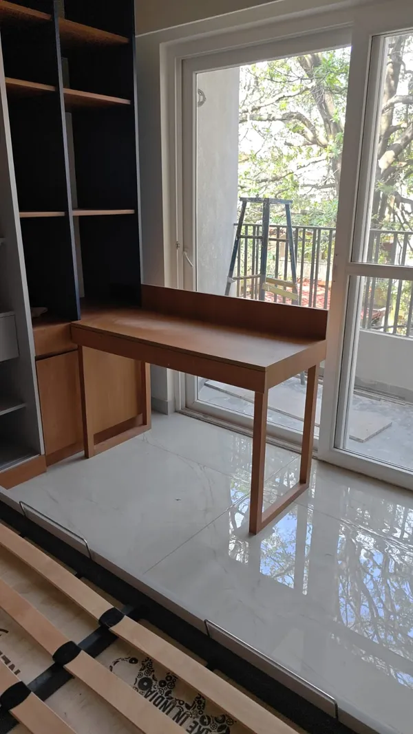 Custom wooden study desk integrated with tall open bookcase beside balcony glass sliding doors
