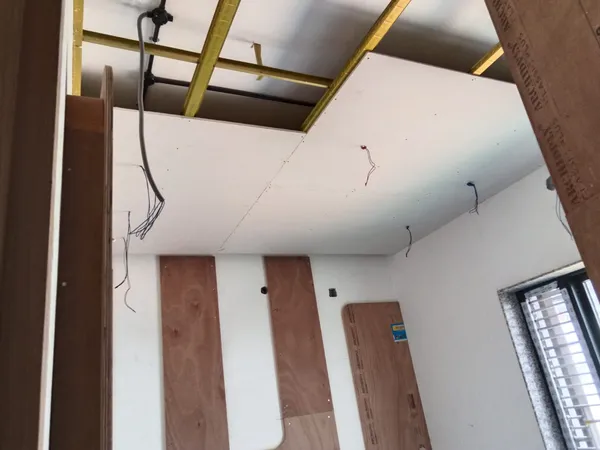 Bedroom ceiling showing metal channel framing, gypsum board installation, and electrical lighting drops